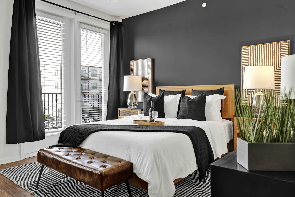Bedroom with a dark accent wall, crisp white bedding, and a leather bench