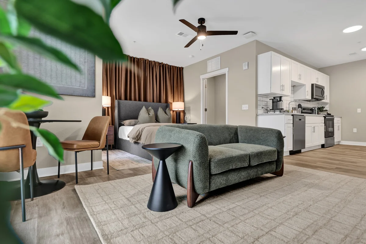 Modern furnished apartment with a green sofa, warm curtains, and an adjoining bedroom